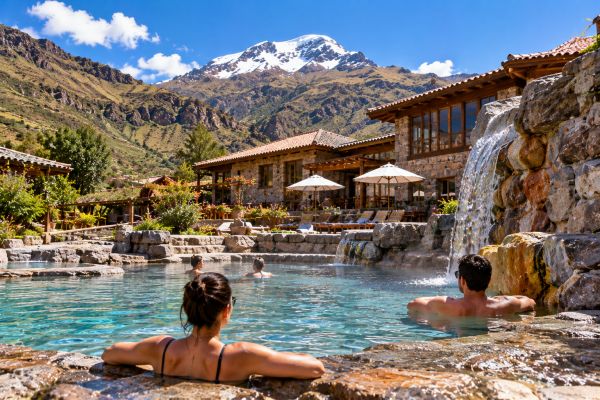 Travelers relaxing in an outdoor thermal pool at Hostería Puente del Inca, surrounded by breathtaking Andean mountain scenery, enjoying a peaceful rest day during their mountaineering expedition.