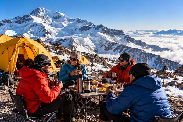 Mountaineers enjoying breakfast at Nido de Cóndores high-altitude camp on Aconcagua, Argentina, surrounded by expedition tents, snow-covered Andean peaks, and spectacular mountain scenery.