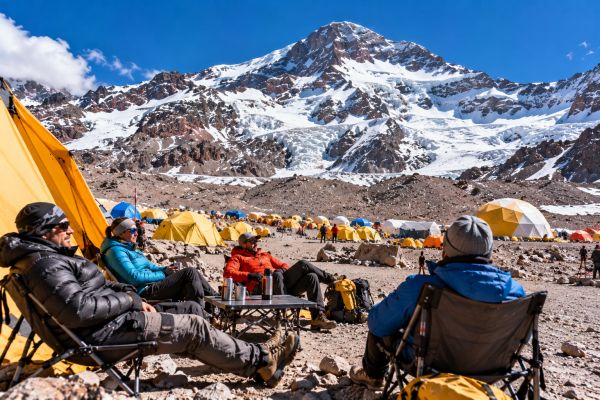 Mountaineers resting at Plaza de Mulas Base Camp on Aconcagua in Argentina, surrounded by expedition tents, rugged Andean landscapes, and spectacular snow-covered mountain peaks.