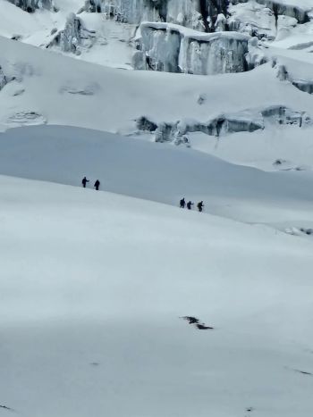 A roped team of mountaineers traverses a vast, snow-covered glacier and ice wall formation on Cotopaxi Volcano, Ecuador.
