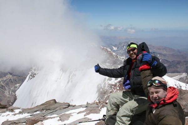 Mountaineers celebrate near the summit of Mount Aconcagua, giving a thumbs up with a dramatic, cloud-filled backdrop over the Andes in Mendoza, Argentina.