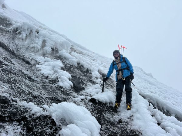 A climber equipped with ice axes and technical gear pauses on a steep, snow-covered glacier slope of Cotopaxi Volcano in Ecuador.
