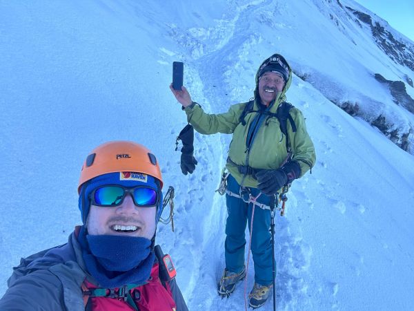 Two climbers celebrate on the snowy glacier slopes of Cotopaxi Volcano in Ecuador, posing for a selfie during a high-altitude mountaineering ascent.