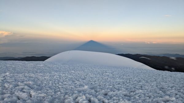 The iconic triangular mountain shadow of Mount Chimborazo projected onto the cloud layer and horizon at sunrise from its icy summit in Ecuador.