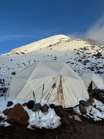 White dome tents set up in snow and rocks at Mount Chimborazo High Camp, framed by the towering snow-covered summit in Ecuador.
