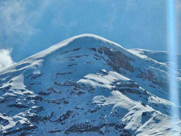 A close-up view of the rounded, snow-covered summit dome and frozen rock ledges of Mount Chimborazo under a clear blue sky in Ecuador.
