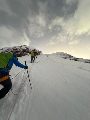 A roped team of climbers ascends a steep, snow-covered glacier slope toward the high ridges of Mount Chimborazo, Ecuador, during early morning light.