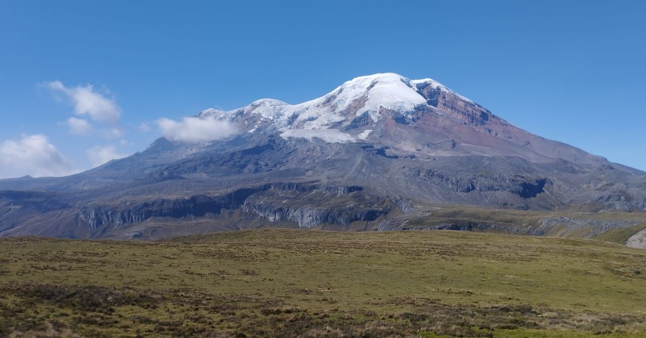 A sweeping panoramic view of Mount Chimborazo's snow-covered summit and massive glacier system rising above the open Andean paramo grasslands in Ecuador.