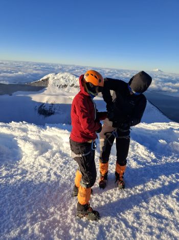 A mountain guide helps a climber adjust safety harnesses on the snow glacier of Cotopaxi Volcano above a sea of clouds in Ecuador.