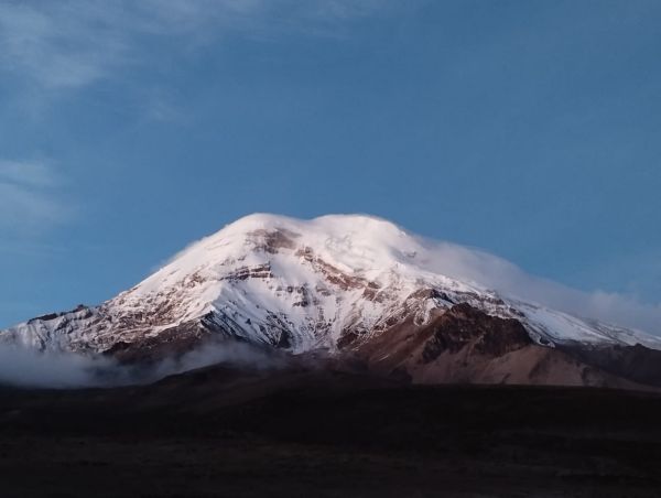 The snow-covered peak of Mount Chimborazo stands majestically above low clouds during dawn in the Ecuadorian Andes.