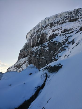 A dramatic view of a rugged rock wall covered in hanging icicles and glacier ice on Cotopaxi Volcano in the Ecuadorian Andes.