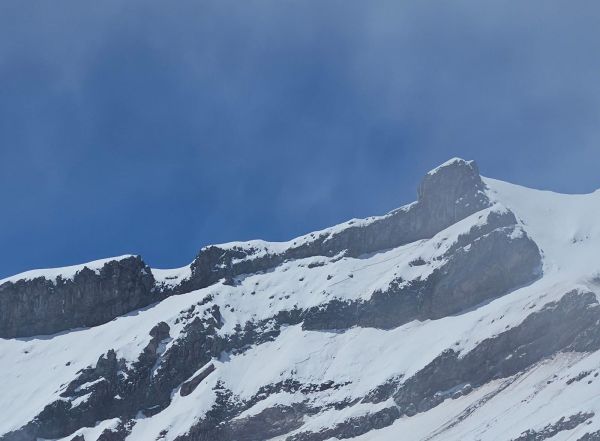 A close-up view of dark, snow-dusted rock ridges and glacial cliffs on Mount Chimborazo under a clear blue sky in Ecuador.