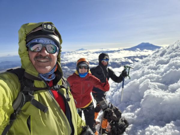 A team of mountaineers taking a selfie on the snowy glacier of Cotopaxi Volcano with dramatic clouds and distant Andean peaks behind them in Ecuador.