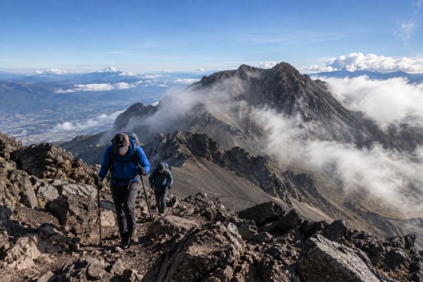 Hikers climb the rocky summit ridge of Rucu Pichincha Volcano (4,796m / 15,724ft) during an acclimatization trek with views of Cotopaxi Volcano near Quito, Ecuador.