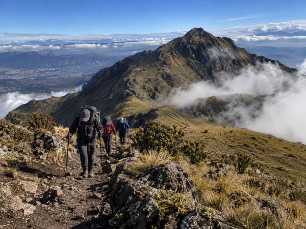 Hikers trek along the scenic ridge trail of Pasochoa Volcano (4,199m / 13,773ft) surrounded by Andean mountain landscapes during an acclimatization hike in Ecuador.